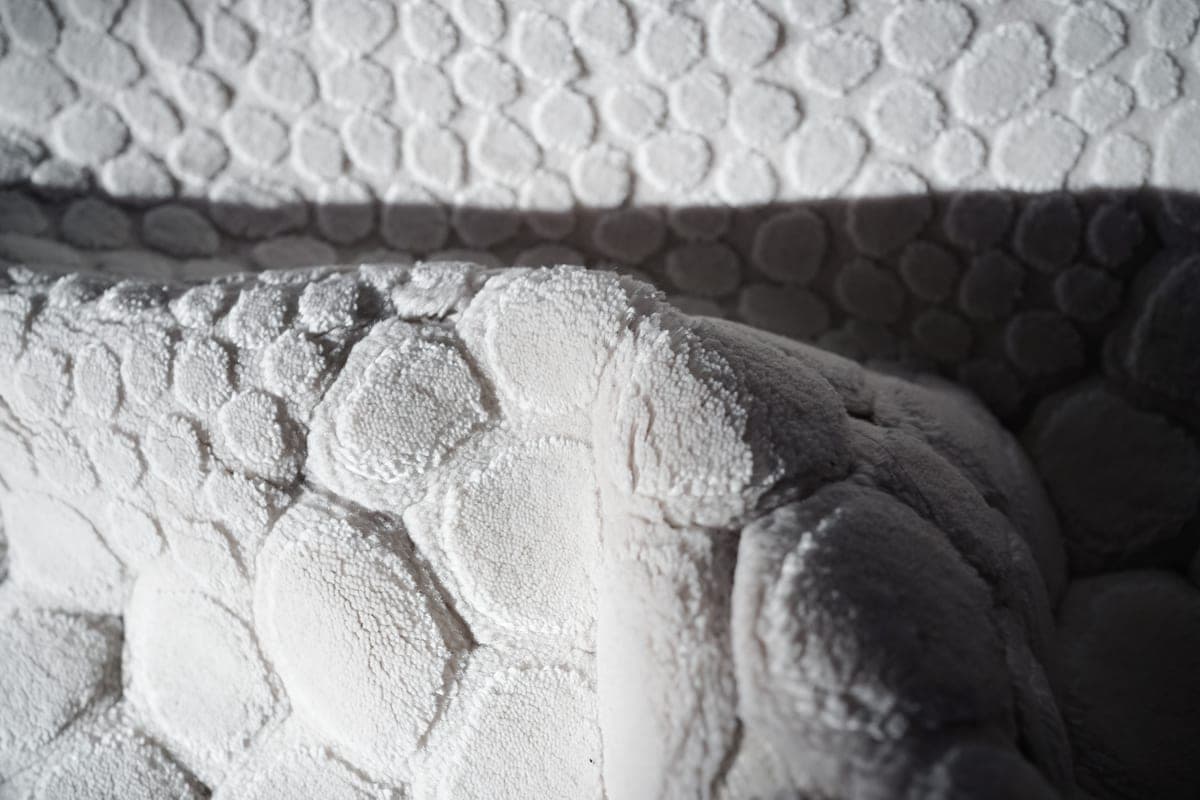 A thick chenille bath mat on the floor beside a bathtub